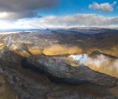 From above columns of smoke and magma sparks out of the volcano hole and run like rivers of lava over the ground in Iceland — Stock Photo