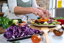 Crop unrecognizable female with raw carrot preparing vegetarian food in the house modern kitchen — Stock Photo