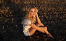 Спокійна жінка в елегантній сукні сидить на сухому полі в сільській місцевості і дивиться на камеру — стокове фото