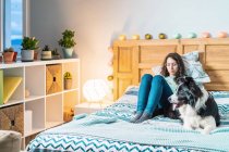 Молода жінка в окулярах сидить на ліжку з прикордонним собакою — стокове фото