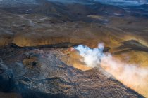 Сверху столбы дыма и магмы искрит из вулканической ямы и течет, как реки лавы над землей в Исландии — стоковое фото