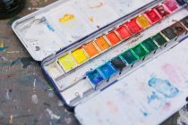 From above of watercolor paint palettes and abstract pictures arranged on table in creative studio — Stock Photo