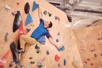 Low angle of muscular male alpinist hanging on climbing wall while training in bouldering center — Stock Photo