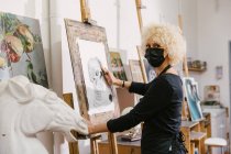 Вид збоку талановитої художниці, що стоїть на мольберті і малює на папері з олівцем в художній студії — стокове фото