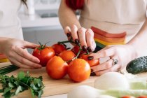 Урожай невизначених жінок, що стоять за столом з різноманітними свіжими овочами для здорового салату під час приготування обіду на кухні — стокове фото