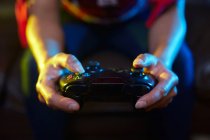 Ritaglia giocatore irriconoscibile utilizzando pad gioia e giocare al videogioco in camera oscura — Foto stock