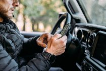 Вид на нерозпізнаного чоловіка, який використовує свій мобільний телефон всередині автомобіля, перш ніж почати водити машину — стокове фото