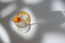 Вид зверху на прозорий келих коктейлю з високим м'ячем, прикрашений цитрусовою плодовою цедрою і гвоздикою проти тіней на сонячному світлі — стокове фото