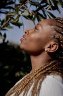Vue latérale de la femme afro-américaine en tenue denim tendance debout dans un jardin verdoyant en été et regardant ailleurs — Photo de stock