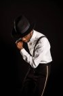 Young masculine ethnic male model in hat and trousers standing dancing on black background — Stock Photo
