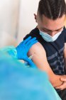 Обрезание женщин-медиков в защитной форме, латексных перчатках и маске для лица вакцинация испанского пациента в клинике во время вспышки коронавируса — стоковое фото
