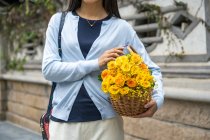 Das Mädchenporträt der schönen Asiatin, während sie einen Weidenkorb mit gelben Blumen trägt. — Stockfoto