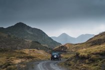 Современный автомобиль едет по пыльной тропе в зеленых горах Пиренеев с лесом в Испании — стоковое фото