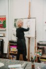 Female artist creating drawing of human with pencil while standing at easel in studio — Stock Photo