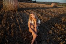 Friedliches Weibchen in elegantem Kleid sitzt auf trockenem Feld im ländlichen Raum und blickt in die Kamera — Stockfoto