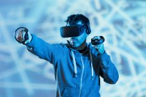 Anonymous unshaven male in hoodie and modern goggles with controllers and extended arm experiencing virtual reality — Stock Photo