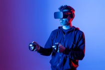 Homem sem barba anônimo com capuz e óculos modernos com controladores e braço estendido experimentando realidade virtual — Fotografia de Stock