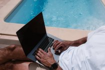 Нерозпізнаний чоловік-фрілансер лежачи на вулиці біля агрегату і серфінг Інтернету на ноутбуці під час телероботи влітку в сонячний день. — стокове фото