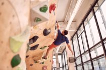 Low angle of muscular male alpinist hanging on climbing wall while training in bouldering center — Stock Photo