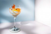 Bicchiere trasparente di cocktail highball decorato con scorza di agrumi e chiodi di garofano contro le ombre alla luce del sole — Foto stock