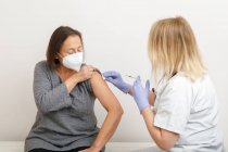 Жінка-медик у захисному одязі та латексних рукавичках вакцинує старшого пацієнта в клініці під час спалаху коронавірусу — стокове фото