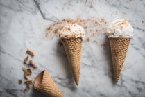 Vista aérea de sabrosos conos de gofre con cremosas cucharadas de gelato de leche merengue en la mesa de mármol - foto de stock
