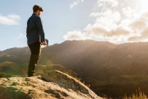 Vista lateral del tranquilo explorador masculino con la tableta de pie en la roca y disfrutar de una vista espectacular de las montañas en el día soleado - foto de stock