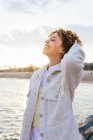 Angle élevé de joyeuse femme afro-américaine debout avec les bras tendus sur les rochers sur le bord de la mer et jouissant de la liberté au coucher du soleil — Photo de stock