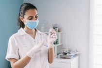 Female doctor in latex gloves and face shield filling in syringe from bottle with vaccine preparing to vaccinate patient in clinic during coronavirus outbreak — Stock Photo