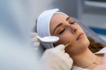 Анонимный культивист-косметолог наносит кислотный пилинг на лицо клиентки во время посещения клиники красоты — стоковое фото