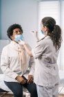 Female medical specialist in protective uniform, latex gloves and face mask doing nasal coronavirus test on African American mature woman patient in clinic during virus outbreak — Stock Photo