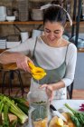 Content female squeezing lemon juice on chard leaves in blender bowl while preparing healthy drink in house kitchen — Stock Photo
