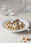 Аппетитные традиционные испанские тушеные белые ткани фасоль с моллюсками в тарелке со свежими листьями петрушки на скатерти — стоковое фото