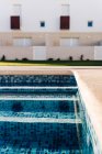 Moderne Häuserfassaden gegen Schwimmbad mit plätscherndem Wasser und Rasen unter blauem Himmel in der Stadt — Stockfoto