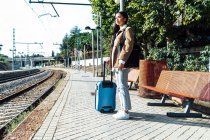 Vista lateral do viajante asiático feminino com mala em pé na plataforma da estação ferroviária enquanto espera o trem — Fotografia de Stock