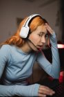 Seitenansicht einer besorgten Spielerin mit Kopfhörer, die ein Videospiel spielt, während sie am Tisch mit der Tastatur sitzt — Stockfoto