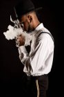 Side view of masculine African American male in white shirt and hat exhaling vapor while smoking e cigarette — Stock Photo
