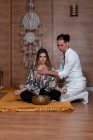 Zen-Lehrer in weißer Kleidung berührt Brust einer Frau mit gekreuzten Beinen während Yoga-Praxis in der Nähe des Schüsselgong — Stockfoto