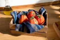 High angle of fresh ripe red tomatoes placed on natural wooden tray with napkin in home kitchen — Stock Photo