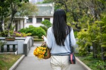 Hermosa chica asiática retrato en un parque mientras ella lleva una canasta de mimbre con flores amarillas. - foto de stock