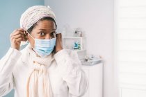 Afro-americano mulher madura paciente com máscara facial sentado na cama clínica à espera de consulta durante a consulta durante o surto de coronavírus — Fotografia de Stock