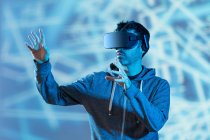 Homme barbu méconnaissable en sweat à capuche et casque moderne explorant la réalité virtuelle sous la lumière du néon — Photo de stock
