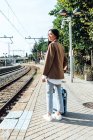 Side view of Asian female traveler with suitcase standing on platform of railroad station while waiting for the train — Stock Photo