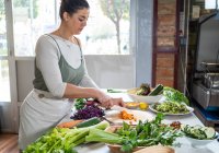 Vista laterale del taglio femminile di carote crude con coltello mentre si prepara cibo vegetariano in cucina moderna — Foto stock