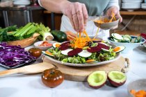 Cultivo hembra irreconocible con zanahoria cruda preparando comida vegetariana en la casa cocina moderna - foto de stock