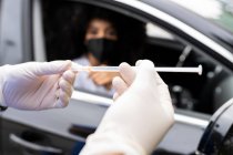 Cropped unrecognizable nurse in latex gloves and uniform preparing to vaccinate African American female patient inside the car on a drive through mobile clinic during coronavirus outbreak — Stock Photo