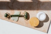 Vista superior do rolo de jade, raspador de guasha e creme facial natural dispostos em mesa de mármore para o conceito de massagem facial — Fotografia de Stock