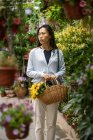 Hermosa chica asiática comprando flores en la tienda de flores mientras lleva una canasta de mimbre con flores amarillas. - foto de stock