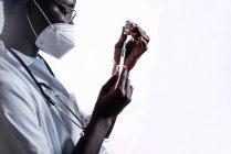 Medico etnico che riempie la siringa dal flacone con il vaccino che si prepara a vaccinare il paziente in background bianco in una clinica durante l'epidemia di coronavirus — Foto stock