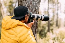 Vista lateral de un fotógrafo aventurero tomando fotos en la montaña con fondo borroso - foto de stock